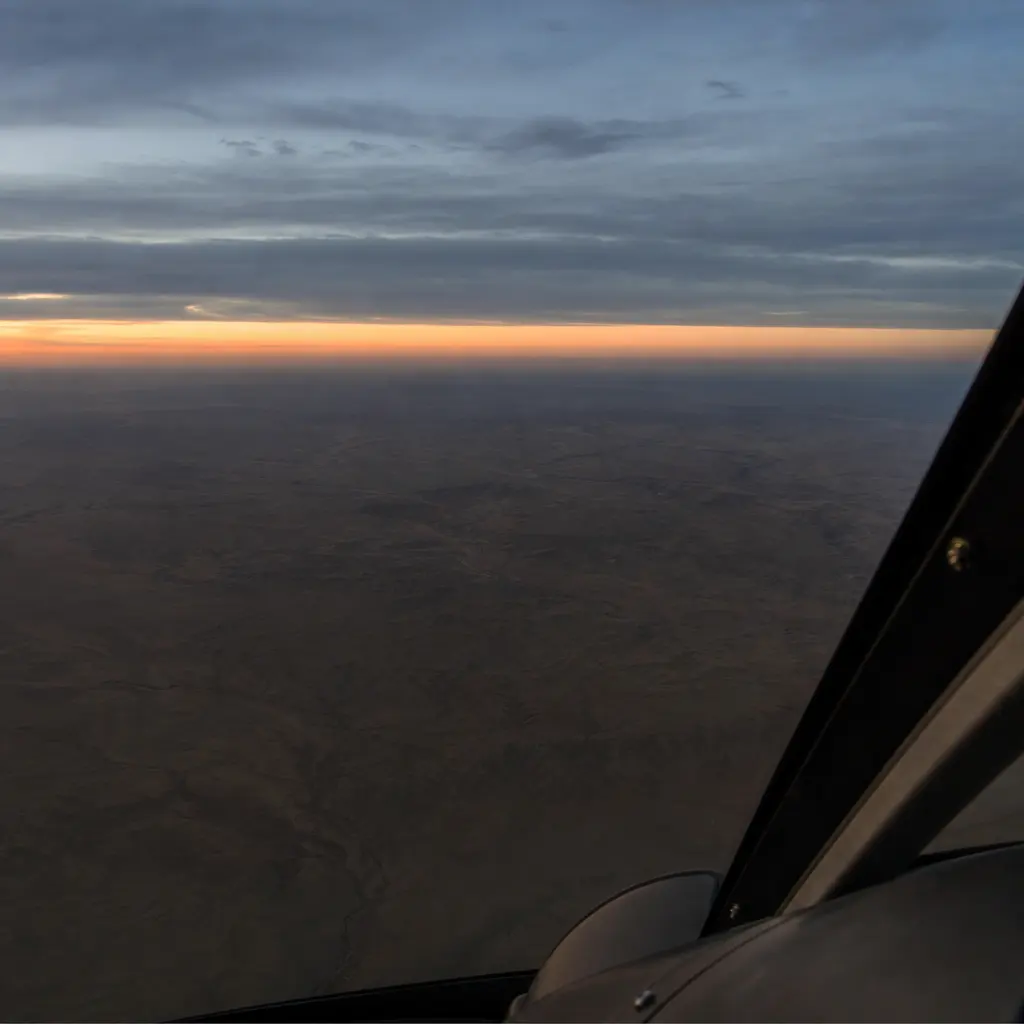 Looking down from a cockpit over featureless desert at dusk, with no roads or landmarks in view
