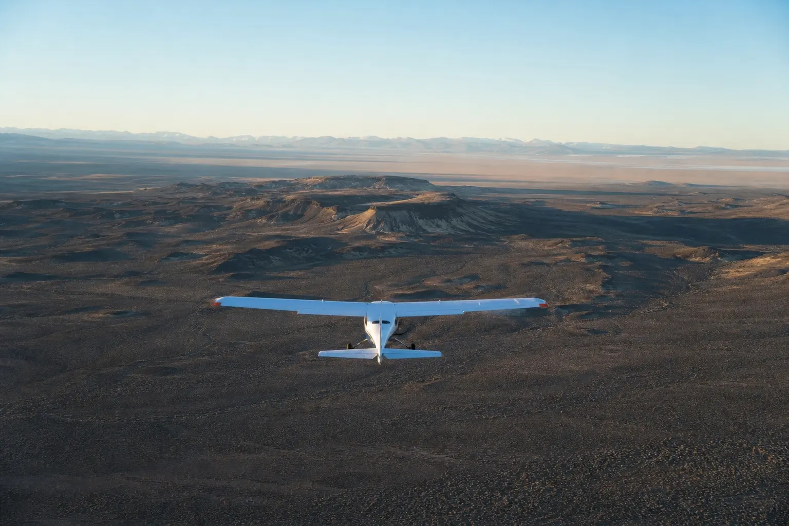 A light survey aircraft flying a straight transect over empty high desert terrain at golden hour