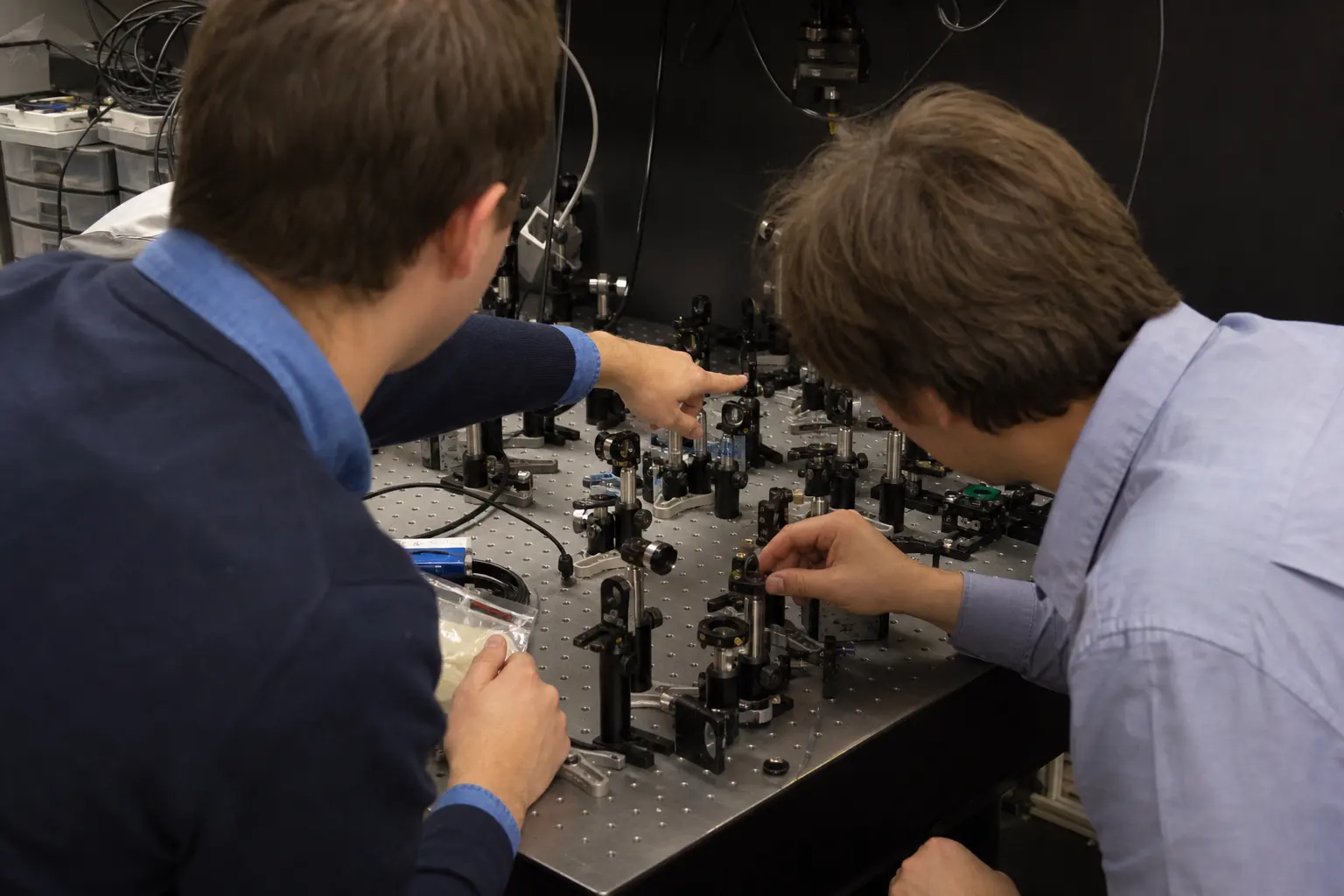 Two engineers at an optics bench covered with mounts, mirrors and cabling, working on an alignment together